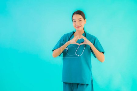 Téléchargez les photos : Portrait belle jeune asiatique médecin femme heureux sourire montrer forme de coeur pour le travail à l'hôpital et la clinique sur fond bleu isolé - en image libre de droit