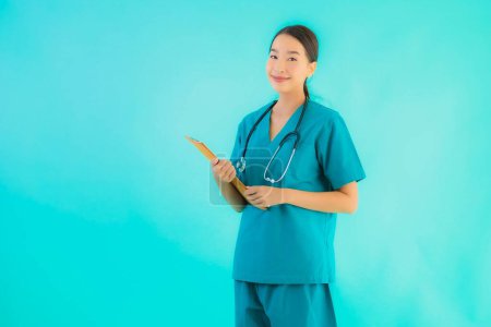 Foto de Retrato hermosa joven asiática médico mujer con tablero de papel vacío para el espacio de copia sobre fondo azul aislado - Salud en el hospital y el concepto de clínica - Imagen libre de derechos