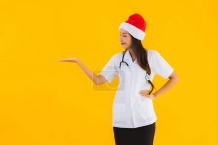 Foto de Retrato hermosa joven asiático médico mujer desgaste navidad o santa sombrero en amarillo aislado fondo - Imagen libre de derechos