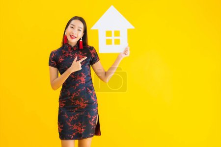 Photo for Portrait beautiful young asian woman wear chinese dress show home sign symbol on yellow isolated background - Royalty Free Image