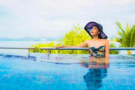 Foto de Retrato hermosa joven mujer asiática relajarse sonrisa ocio alrededor de piscina al aire libre con vista al mar océano para vacaciones de viaje - Imagen libre de derechos