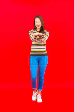 Téléchargez les photos : Portrait belle jeune femme asiatique sourire avec action sur fond rouge isolé - en image libre de droit
