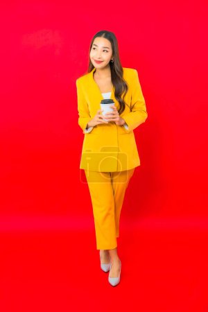 Téléchargez les photos : Portrait belle jeune femme d'affaires asiatique avec tasse de café sur fond rouge - en image libre de droit