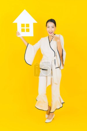 Photo for Portrait beautiful young business asian woman with home paper sign on yellow background - Royalty Free Image