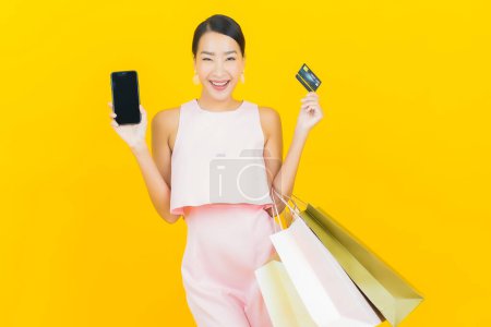Téléchargez les photos : Portrait belle jeune femme asiatique sourire avec sac à provisions sur fond de couleur jaune - en image libre de droit