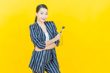 Téléchargez les photos : Portrait belle jeune femme asiatique avec maquillage pinceau cosmétique sur fond de couleur - en image libre de droit