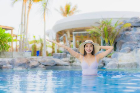 Téléchargez les photos : Portrait belle jeune femme asiatique sourire heureux se détendre autour de la piscine extérieure dans la station hôtelière pour les vacances de loisirs - en image libre de droit