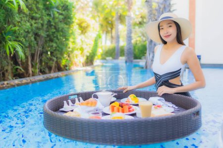 Téléchargez les photos : Portrait belle jeune femme asiatique sourire heureux avec petit déjeuner flottant dans le plateau sur la piscine - en image libre de droit