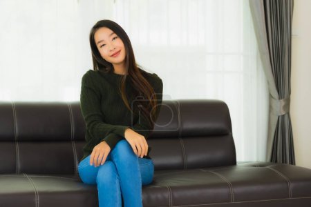 Téléchargez les photos : Beau portrait jeune femme asiatique assis se détendre sur le canapé dans le salon intérieur - en image libre de droit