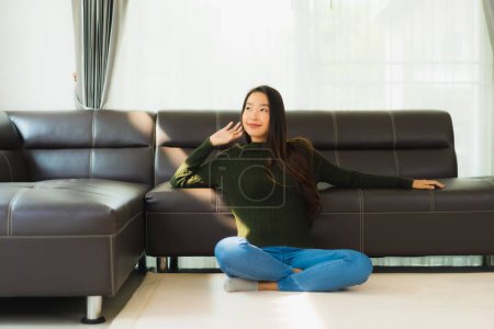 Téléchargez les photos : Beau portrait jeune femme asiatique assis se détendre sur le canapé dans le salon intérieur - en image libre de droit