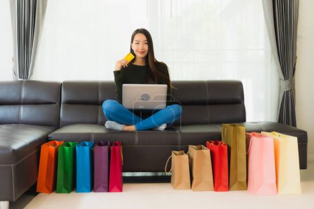 Téléchargez les photos : Portrait belle jeune femme asiatique utiliser ordinateur portable et carte de crédit avec sac à provisions pour les achats en ligne à la maison - en image libre de droit