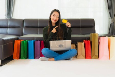 Téléchargez les photos : Portrait belle jeune femme asiatique utiliser ordinateur portable et carte de crédit avec sac à provisions pour les achats en ligne à la maison - en image libre de droit