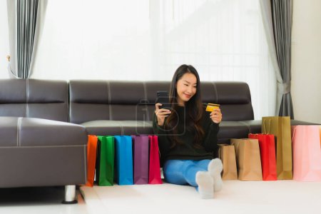 Foto de Retrato hermosa mujer asiática joven con bolsa de compras y tarjeta de crédito con teléfono móvil para las compras en línea en casa - Imagen libre de derechos