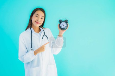 Foto de Retrato hermosa joven asiática médico mujer con reloj o alarma en azul aislado fondo - Imagen libre de derechos