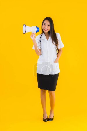 Téléchargez les photos : Portrait belle jeune asiatique médecin femme utiliser mégaphone sur fond jaune isolé - en image libre de droit