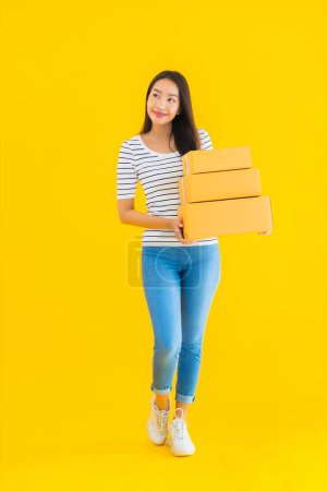 Foto de Retrato hermosa joven mujer asiática con caja de paquete listo para el envío sobre fondo aislado amarillo - Imagen libre de derechos