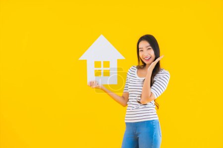 Téléchargez les photos : Portrait belle jeune femme asiatique montrer maison signe papier sur fond jaune isolé - en image libre de droit