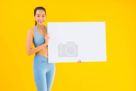 Téléchargez les photos : Portrait belle jeune femme asiatique porter des vêtements de sport montrer vide panneau d'affichage blanc sur fond jaune isolé - en image libre de droit