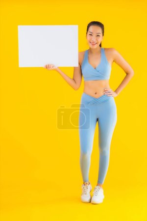 Photo for Portrait beautiful young asian woman wear sportwear show empty white billboard on yellow isolated background - Royalty Free Image