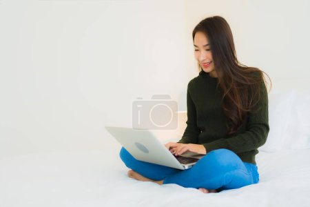 Téléchargez les photos : Portrait belle jeune femme asiatique avec ordinateur portable et tasse de café pour le travail sur le lit dans la chambre à coucher intérieur - en image libre de droit