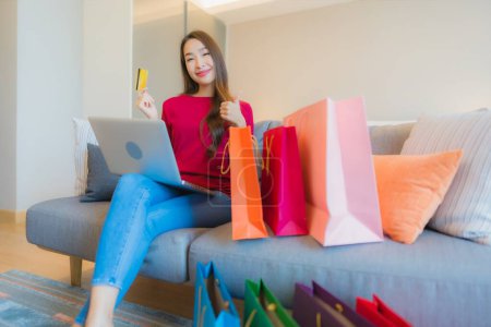 Photo for Portrait beautiful young asian woman use laptop computer with credit card for online shopping with bag on sofa - Royalty Free Image