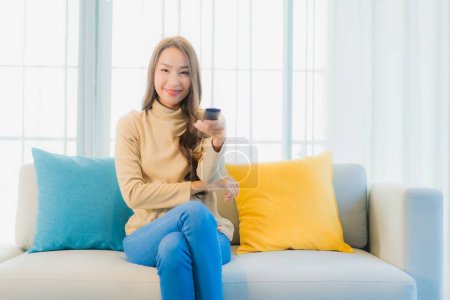 Téléchargez les photos : Portrait belle jeune femme asiatique avec téléviseur sur canapé dans le salon intérieur - en image libre de droit