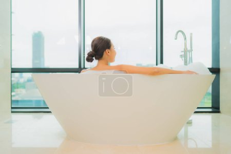 Téléchargez les photos : Portrait belle jeune femme asiatique relax sourire loisirs dans la baignoire dans salle de bain intérieur - en image libre de droit