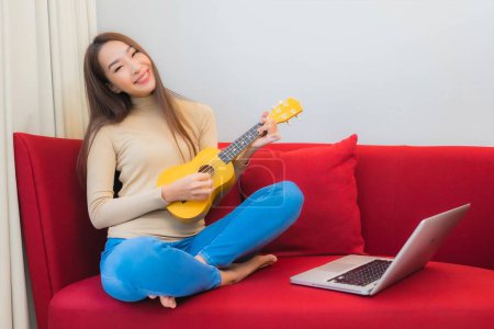 Photo for Portrait beautiful young asian woman play ukulele on sofa in living room interior - Royalty Free Image