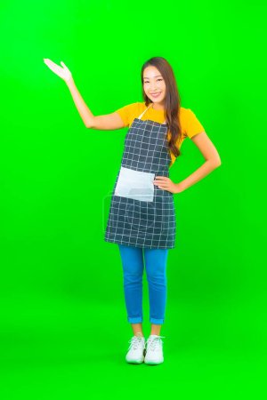 Foto de Retrato hermosa joven mujer asiática usar delantal con acción en verde aislado fondo - Imagen libre de derechos
