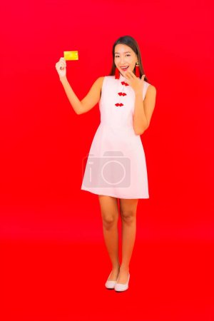 Foto de Retrato hermosa joven asiática mujer con tarjeta de crédito en rojo aislado fondo - Imagen libre de derechos
