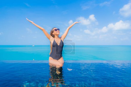 Téléchargez les photos : Portrait belle jeune femme asiatique relax sourire loisirs autour de la piscine extérieure en hôtel station balnéaire avec vue sur mer océan - en image libre de droit
