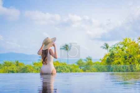 Foto de Retrato hermosa joven mujer asiática disfrutar alrededor de piscina al aire libre con vista al mar en viaje de vacaciones - Imagen libre de derechos