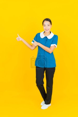 Téléchargez les photos : Portrait belle jeune femme asiatique femme de ménage et sourire avec action sur fond de couleur jaune - en image libre de droit