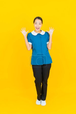 Téléchargez les photos : Portrait belle jeune femme asiatique femme de ménage et sourire avec action sur fond de couleur jaune - en image libre de droit