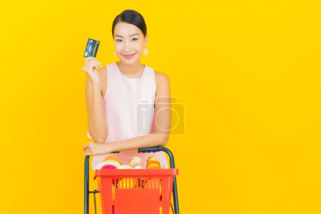 Photo for Portrait beautiful young asian woman smile with grocery basket from supermarket on yellow color background - Royalty Free Image