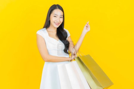 Téléchargez les photos : Portrait belle jeune femme asiatique sourire avec sac à provisions sur fond de couleur jaune - en image libre de droit