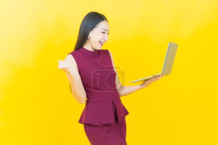 Téléchargez les photos : Portrait belle jeune femme asiatique sourire avec ordinateur portable sur fond isolé - en image libre de droit