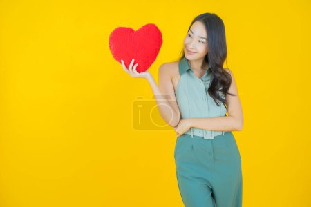 Téléchargez les photos : Portrait belle jeune femme asiatique sourire avec forme d'oreiller de coeur sur fond de couleur - en image libre de droit
