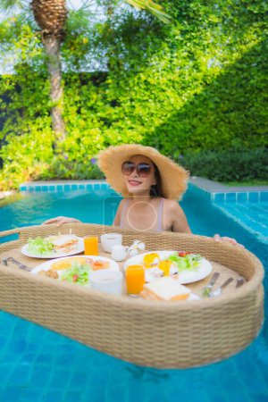 Foto de Retrato joven mujer asiática feliz sonrisa disfrutar con bandeja de desayuno flotante en la piscina en el complejo hotelero - Imagen libre de derechos