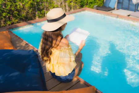 Téléchargez les photos : Portrait jeune femme asiatique lire livre autour de la piscine extérieure dans la station hôtelière - en image libre de droit