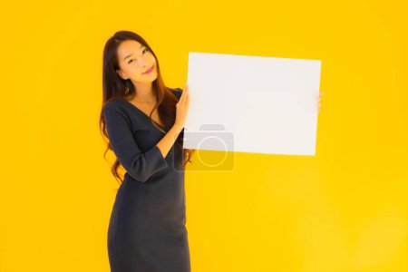 Téléchargez les photos : Portrait belle jeune femme asiatique avec bannière de carte de panneau d'affichage vide et vide sur fond isolé jaune - en image libre de droit