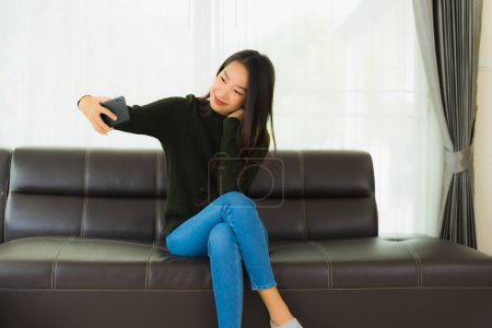 Téléchargez les photos : Portrait belle jeune femme asiatique utiliser téléphone mobile intelligent ou téléphone portable sur canapé dans le salon intérieur - en image libre de droit