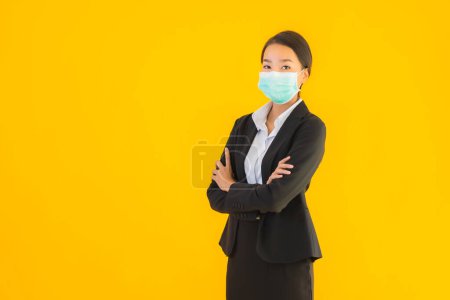 Téléchargez les photos : Portrait belle jeune entreprise asiatique femme porter masque pour protéger covid19 coronavirus sur fond jaune isolé - en image libre de droit
