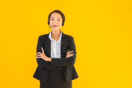 Téléchargez les photos : Portrait belle jeune femme asiatique d'affaires avec casque ou casque pour centre d'appels ou de télémarketing sur fond jaune isolé - en image libre de droit