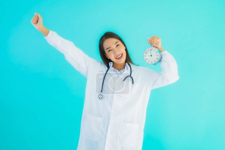 Photo for Portrait beautiful young asian doctor woman with clock or alarm on blue isolated background - Royalty Free Image
