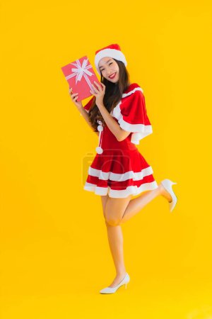 Photo for Portrait beautiful young asian christmas clothes and hat smile happy with red gift box on yellow isolated background - Royalty Free Image