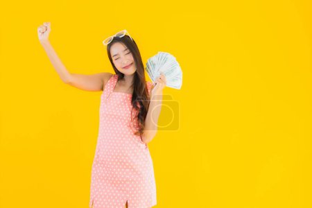 Foto de Retrato hermosa joven asiática mujer mostrar un montón de dinero en efectivo y dinero en amarillo aislado fondo - Imagen libre de derechos