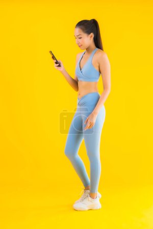 Photo for Portrait beautiful young asian woman wear sportwear with smart mobile phone on yellow isolated background - Royalty Free Image