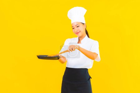 Photo for Portrait beautiful young asian chef woman with black pan on yellow isolated background - Royalty Free Image