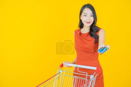 Téléchargez les photos : Portrait belle jeune femme asiatique sourire avec panier d'épicerie du supermarché sur fond de couleur - en image libre de droit